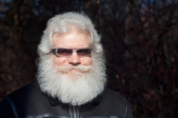 Senior smiling blond caucasian man with splendid beard and moustache wearing sunglasses and looking at camera. Closeup portrait of elderly stylish hipster against dark background.