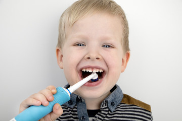 Four year old child brushes his teeth with an electric brush. The boy on a white background laughs...