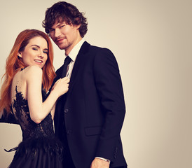 Beautiful happy couple hugging on blue background in evening fashion clothing. Redheaded hairstyle laughing girl holding on black suit her brunette man in studio. Closeup