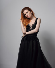 Beautiful elegant young model with bright foxy hairstyle posing in fashion chic black dress with long skirt on studio