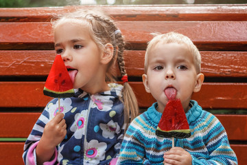 Two kids eating bright red candies with watermelon taste in the park at summer