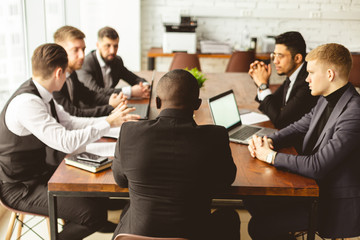 A team of young businessmen in suits working and communicating together in an office. Corporate businessteam and manager in a meeting.