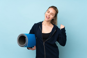 Teenager Russian girl holding mat isolated on blue background celebrating a victory