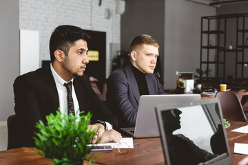 A team of young businessmen in suits working and communicating together in an office. Corporate businessteam and manager in a meeting.