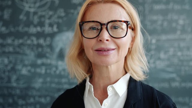 Portrait of attractive adult lady smart professor standing indoors in university class smiling looking at camera. Education, emotions and people concept.