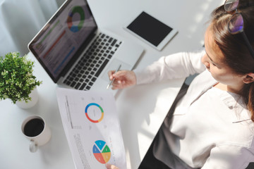 Young employee working at office on laptop while sitting at table, Business woman analyze document in her hands, Graphs and diagram on notebook screen.