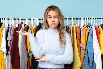 Teenager Russian girl buying some clothes isolated on blue background unhappy for not understand something
