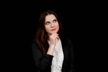 Portrait of young business woman in 
a black jacket is thinking on black background