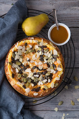Autumn pear pie with pumpkin seeds and almond petals on blue grey wooden table with caramel, top view