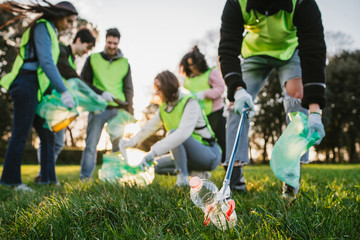 Group of friends during a volunteer garbage collection event in a park at sunset - Millennial...