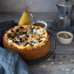 Autumn homemade pear pie with pumpkin seeds and almond petals on wood grey table and coffee cup