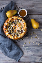 Autumn pear pie with pumpkin seeds and almond petals on blue grey wooden table with caramel, top view