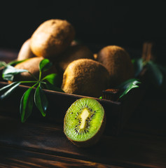 Fresh kiwi fruit with green leaves in an wooden crate on wooden background.