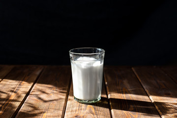 glass of milk on a wooden table. dark background, bright contrasting sun