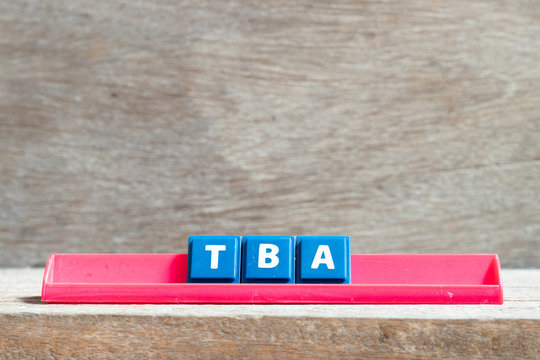 Tile letter on red rack in word TBA (abbreviation of to be announced) on wood background