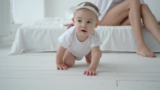 Cute Infant Baby Girl Crawling On Floor While Mom Sitting On Bed