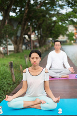 woman and man practicing yoga and meditation on mat near lagoon. health concept.