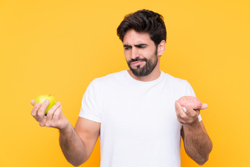 Young handsome man with beard over isolated yellow background having doubts while taking a...