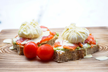 Benedict eggs with avocado and smoked salmon on a wooden board.