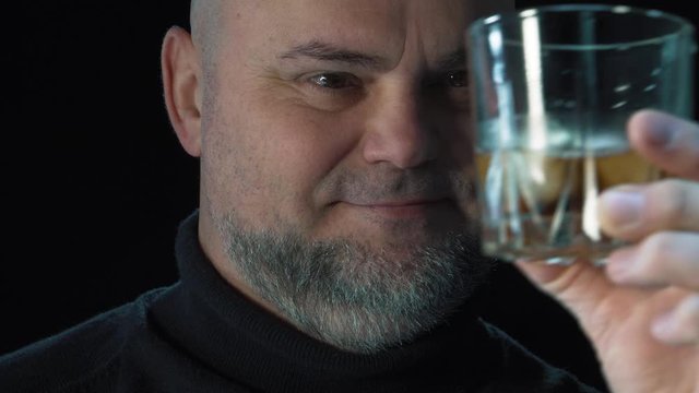 Man winces from strong alcohol  Bearded man drinks  whiskey with ice cubes.  Isolated on black background close up portrait. Alcohol drink and alcohol addiction concept. 
