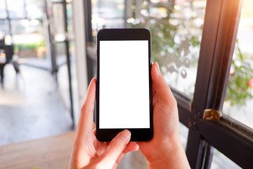 Mockup picture of business woman’s hands holding smart phone with white blank screen in modern place.