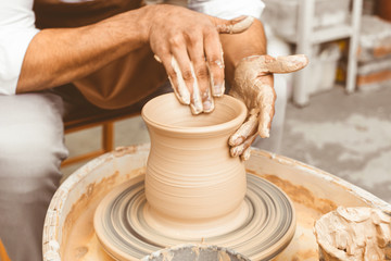 A young male potter works in his workshop on a potter's wheel and makes clay products. Close-up of hands