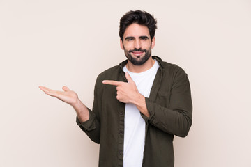 Young handsome man with beard over isolated background holding copyspace imaginary on the palm to...