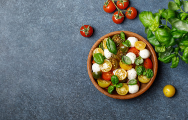 Italian caprese salad with sliced tomatoes, mozzarella cheese, basil, olive oil in wooden bowl. Italian food