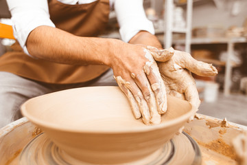 A young male potter works in his workshop on a potter's wheel and makes clay products. Close-up of hands