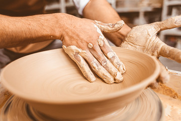 A young male potter works in his workshop on a potter's wheel and makes clay products. Close-up of hands