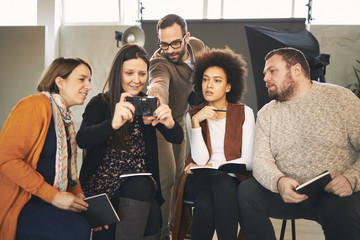 Multicultural attendees of photography class sitting in studio, listening and asking questions about camera parts.