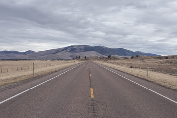 Empty roadway leading line to large rolling hills with sparse tree coverage