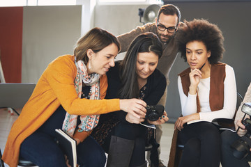 Multicultural attendees of photography class sitting in studio and looking at camera while tutor standing and looking at them.