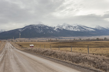 Empty dirt road alongside vintage cattle fencing with large snow capped mountain range