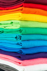 close-up stack of many fresh new fabric cotton t-shirts in colorful rainbow colors. Pile of various...