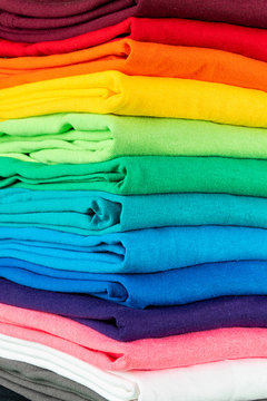 Close-up Stack Of Many Fresh New Fabric Cotton T-shirts In Colorful Rainbow Colors. Pile Of Various Colored Shirts Background