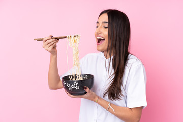 Young brunette woman over isolated pink background holding a bowl of noodles with chopsticks and eating it