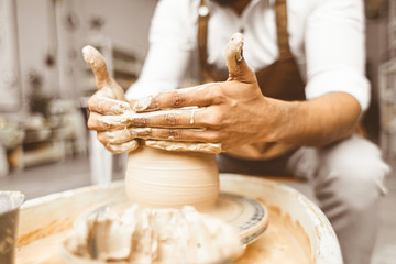 A young male potter works in his workshop on a potter's wheel and makes clay products. Close-up of hands