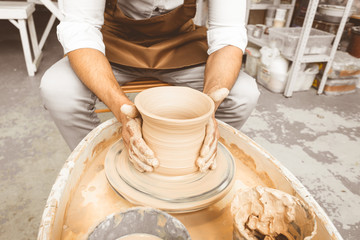 A young male potter works in his workshop on a potter's wheel and makes clay products. Close-up of hands