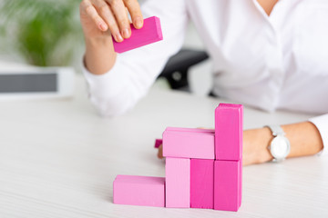 Cropped view of businesswoman stacking pink building blocks on table