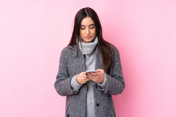 Young brunette woman over isolated pink background sending a message with the mobile