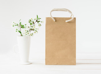 Blank craft package of brown paper,shopping bag with handles.Blooming flowers in vase.White...