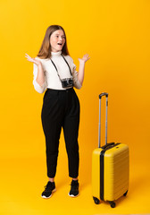 Full body of traveler teenager girl with suitcase over isolated yellow background with surprise facial expression