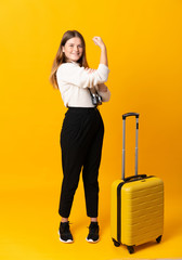 Full body of traveler teenager girl with suitcase over isolated yellow background making strong gesture