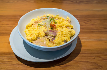 Scrambled eggs with ham and rice in white bowl and white dish on a table.