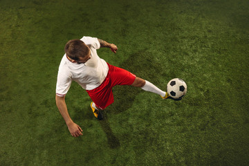 Top view of caucasian football or soccer player on green background of grass. Young male sportive model training, practicing. Kicking ball, attacking, catching. Concept of sport, competition, winning.