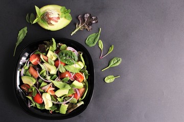 Vegetarian salad of avocado,mints,basil,spinach cherry tomatoes,Spanish onion,lettuce,,arugula. photo isolate on black top view copy space 