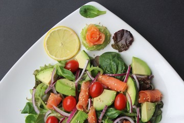 Salmon salad with avocado,cherry tomatoes,Spanish onion,spinach,cucumber noodle, lettuce,sesame seeds,corn salad photo isolate on black top view