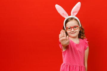 Little girl in easter bunny ears and glasses on a red background. The child shows a stop sign