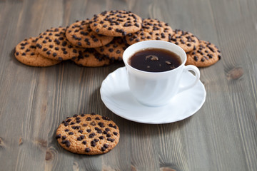 A stack of chocolate chip cookies around coffee cup on a wooden table